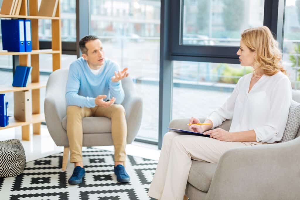 Man and woman engaged in therapy session. Man is talking, woman therapist is listening attentively